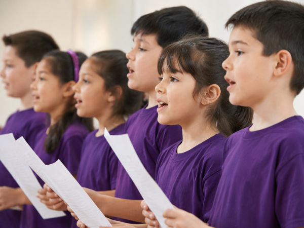Niños y niñas cantando con poleras moradas en una clase de canto infantil